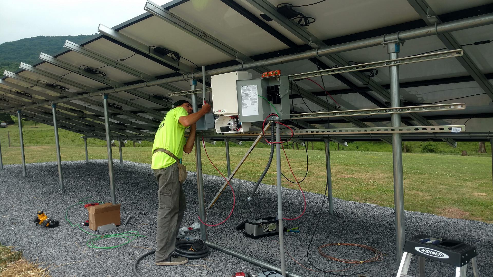 Man examining electrical boxes attached to solar panels